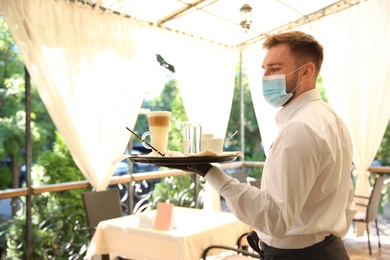 Photo of Waiter serving beverages in restaurant. Catering during coronavirus quarantine