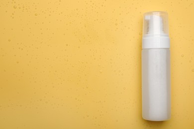 Photo of Wet bottle of face cleansing product on pale orange background, top view. Space for text