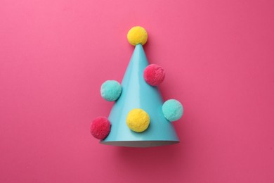 Photo of One light blue party hat with pompoms on pink background, top view