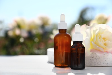 Photo of Bottles of essential oil and fresh rose on table against blurred background. Space for text