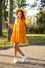 Photo of Beautiful young woman wearing stylish yellow dress and straw hat in park