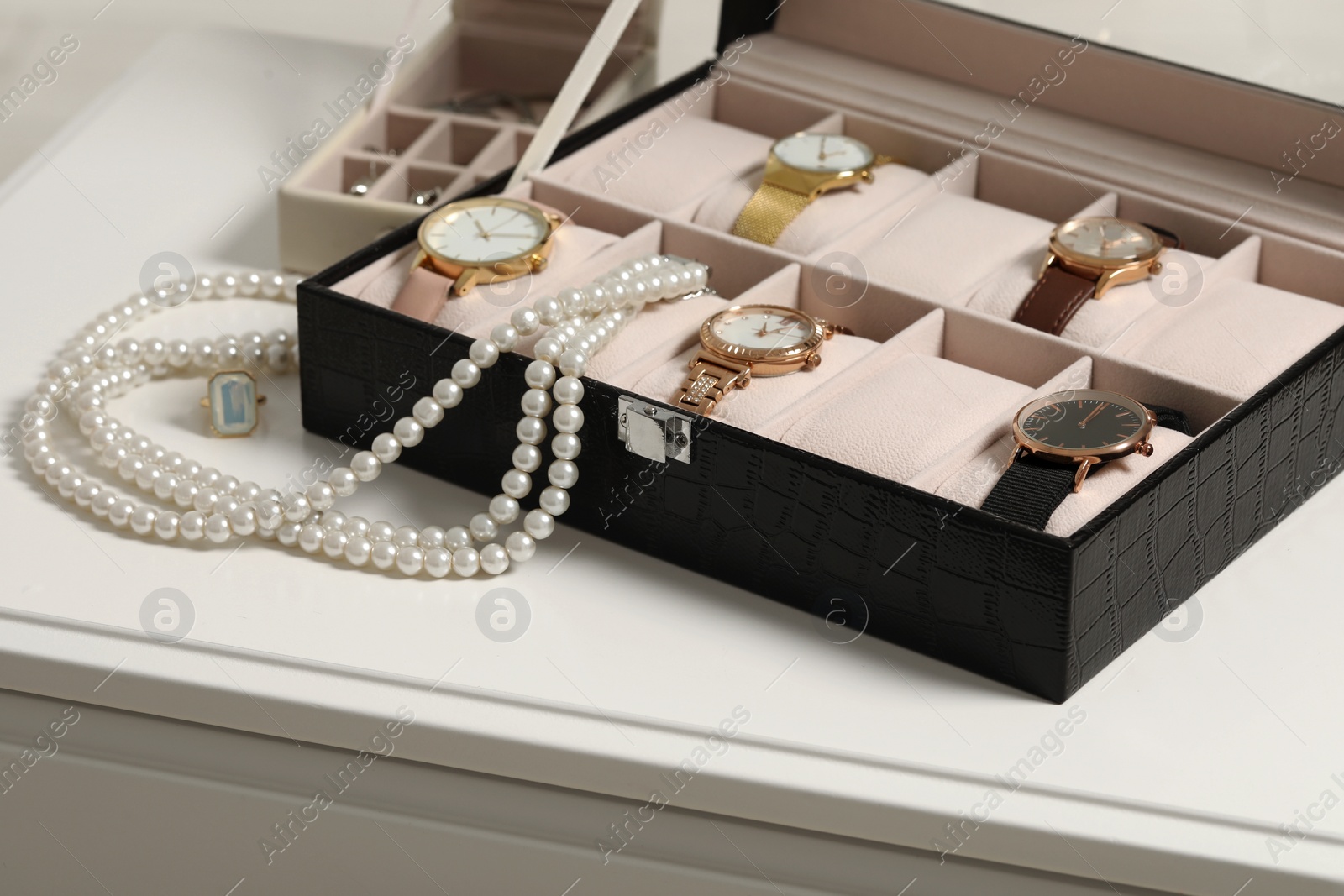 Photo of Jewelry boxes with many stylish wristwatches, accessories and pearl necklace on white table, closeup