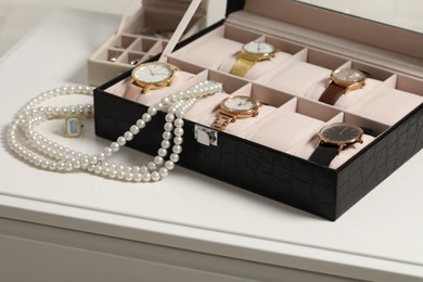 Photo of Jewelry boxes with many stylish wristwatches, accessories and pearl necklace on white table, closeup