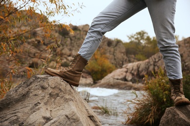 Photo of Woman wearing stylish hiking boots on cliff, closeup