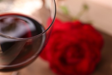 Photo of Glass of red wine and rose flower on blurred background, closeup. Space for text