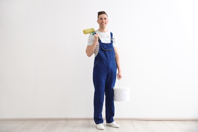 Photo of Young male decorator with paint roller and bucket in empty room