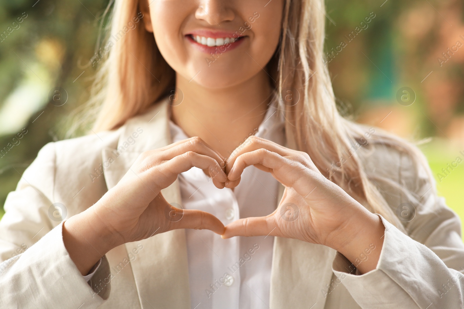 Photo of Woman showing heart gesture with hands against blurred background, closeup. Love concept