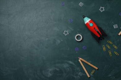 Photo of Bright toy rocket and school supplies on chalkboard, flat lay. Space for text