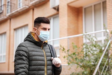 Photo of Man in medical face mask and gloves walking outdoors. Personal protection during COVID-19 pandemic