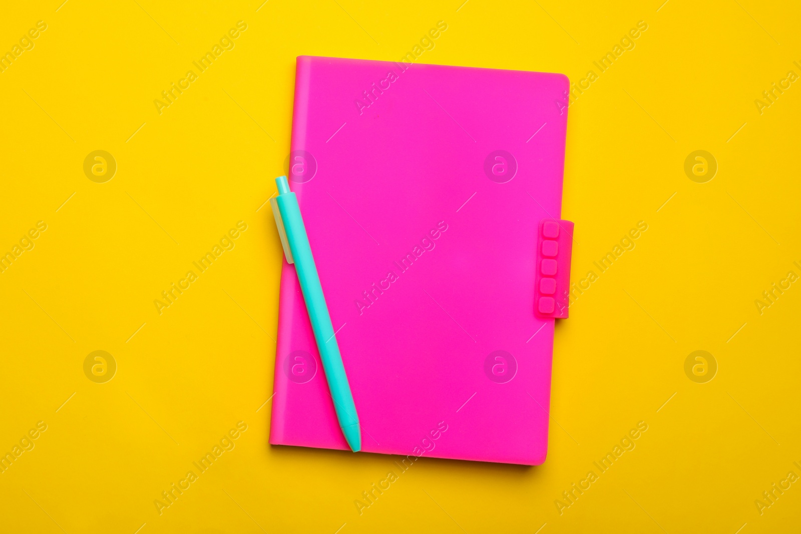 Photo of Pink notebook and pen on yellow background, top view