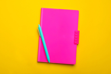 Photo of Pink notebook and pen on yellow background, top view