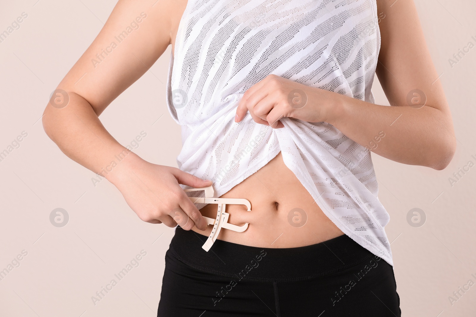 Photo of Young woman measuring body fat with caliper on beige background, closeup. Nutritionist's tool