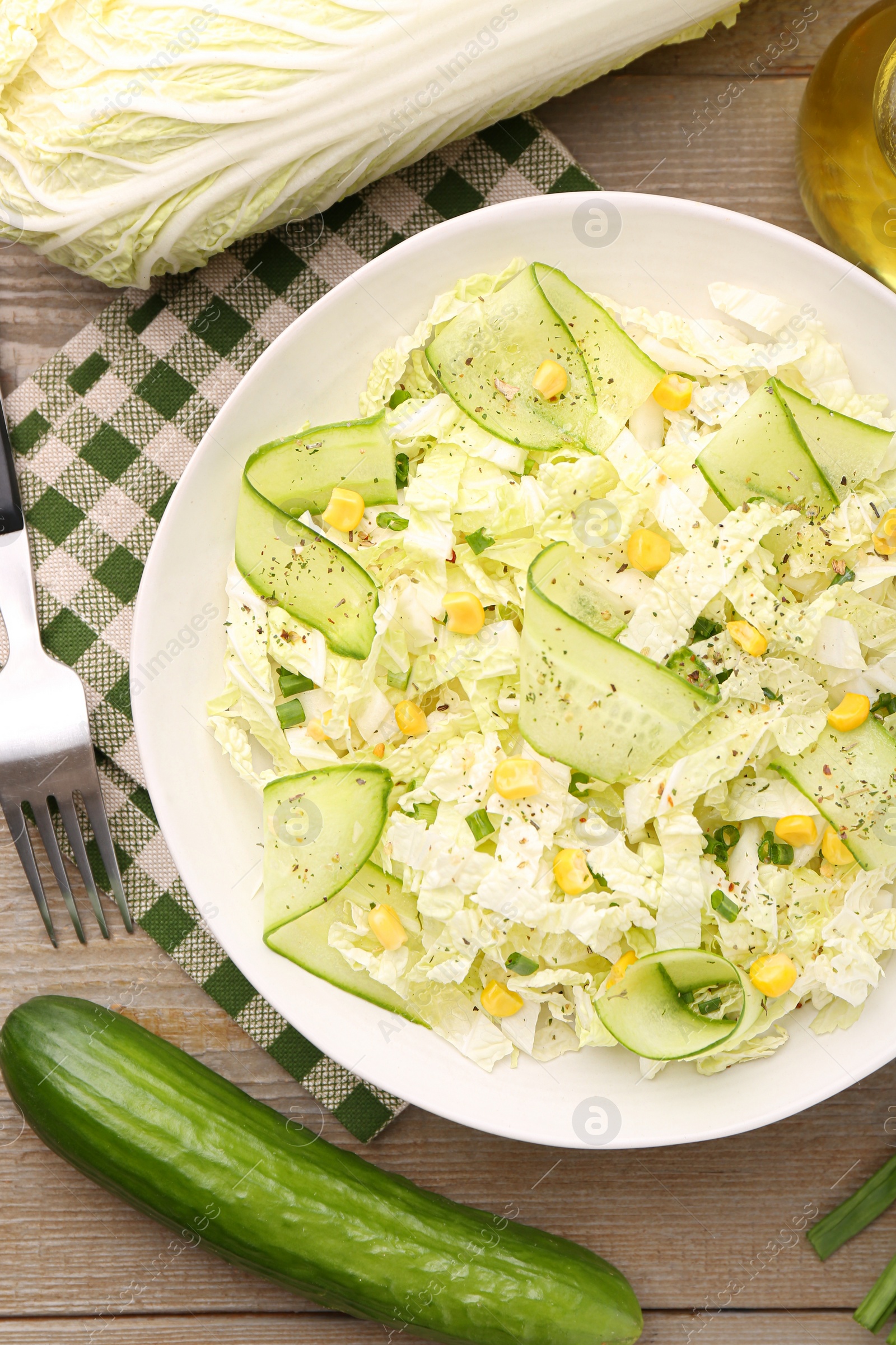 Photo of Tasty salad with Chinese cabbage in bowl and ingredients on wooden table, flat lay