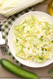 Photo of Tasty salad with Chinese cabbage in bowl and ingredients on wooden table, flat lay