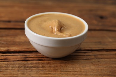 Photo of Delicious nut butter in bowl on wooden table, closeup