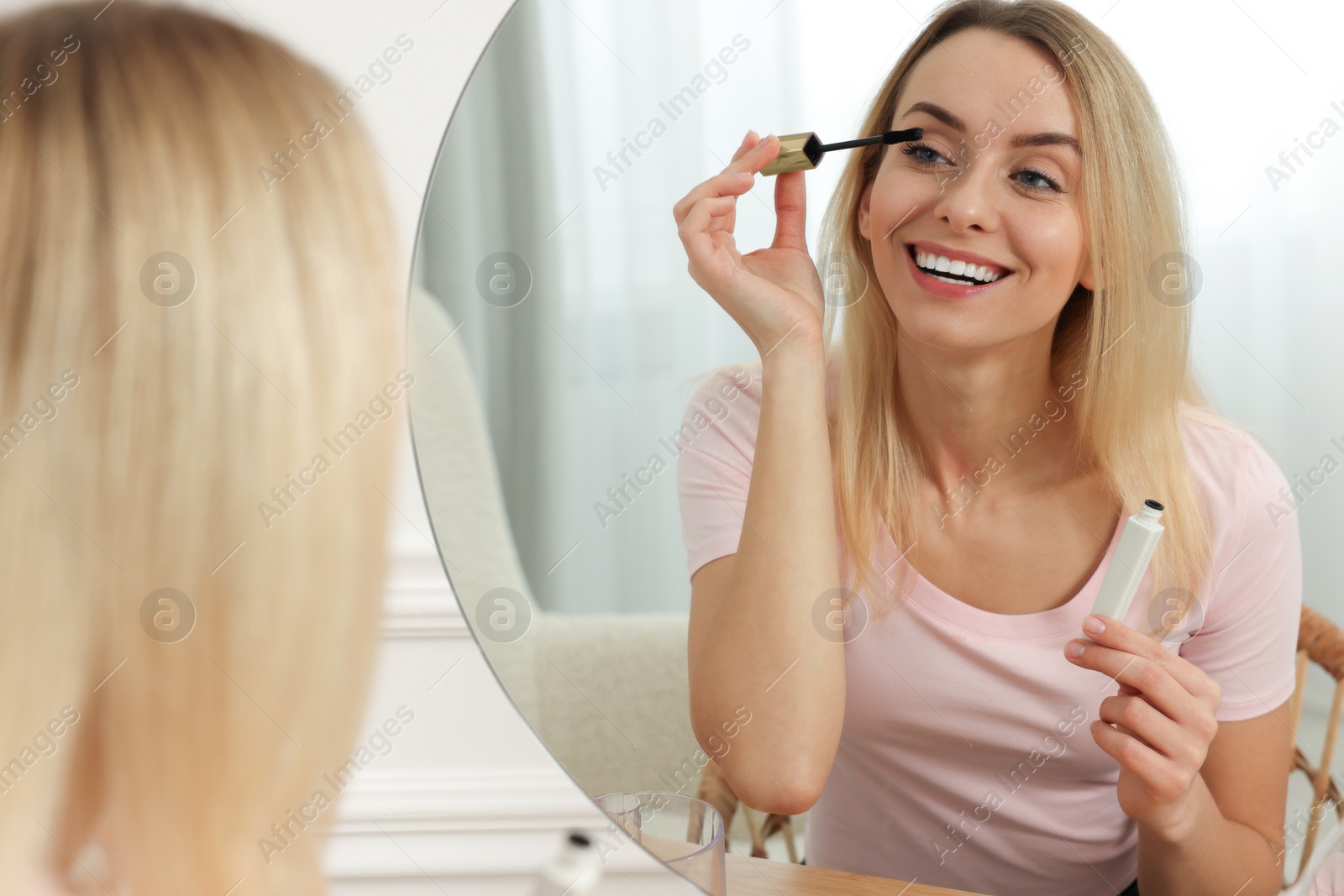 Photo of Beautiful woman applying mascara near mirror at home