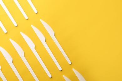 Plastic knives on color background, top view with space for text. Picnic table setting