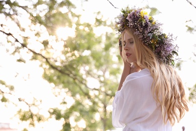 Young woman wearing wreath made of beautiful flowers outdoors on sunny day