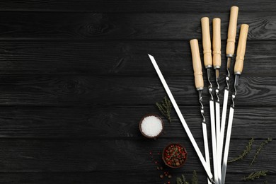 Flat lay composition with metal skewers on black wooden table. Space for text