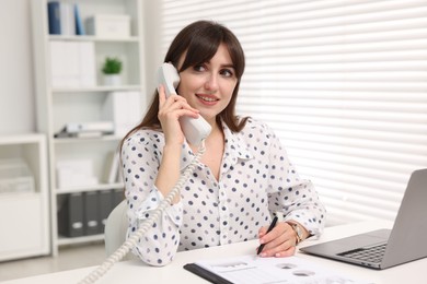 Smiling secretary talking on telephone at table in office