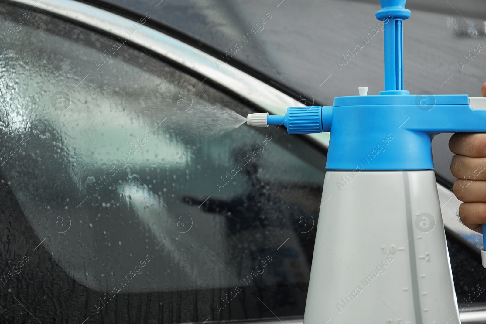 Photo of Worker spraying water onto car window before tinting in workshop, closeup