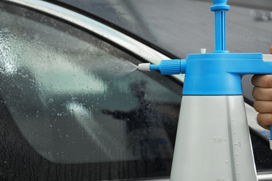 Photo of Worker spraying water onto car window before tinting in workshop, closeup