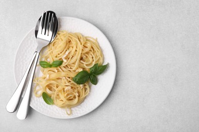 Delicious pasta with brie cheese and basil leaves on light grey table, top view. Space for text