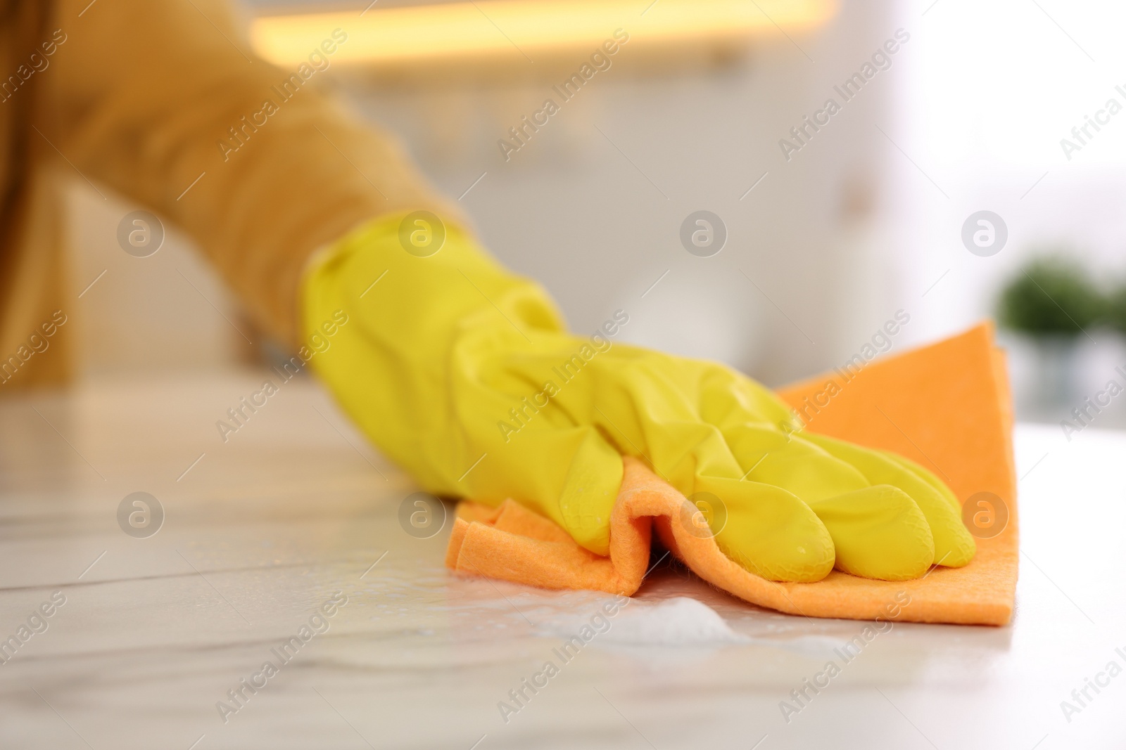 Photo of Woman with microfiber cloth cleaning white marble table in kitchen, closeup