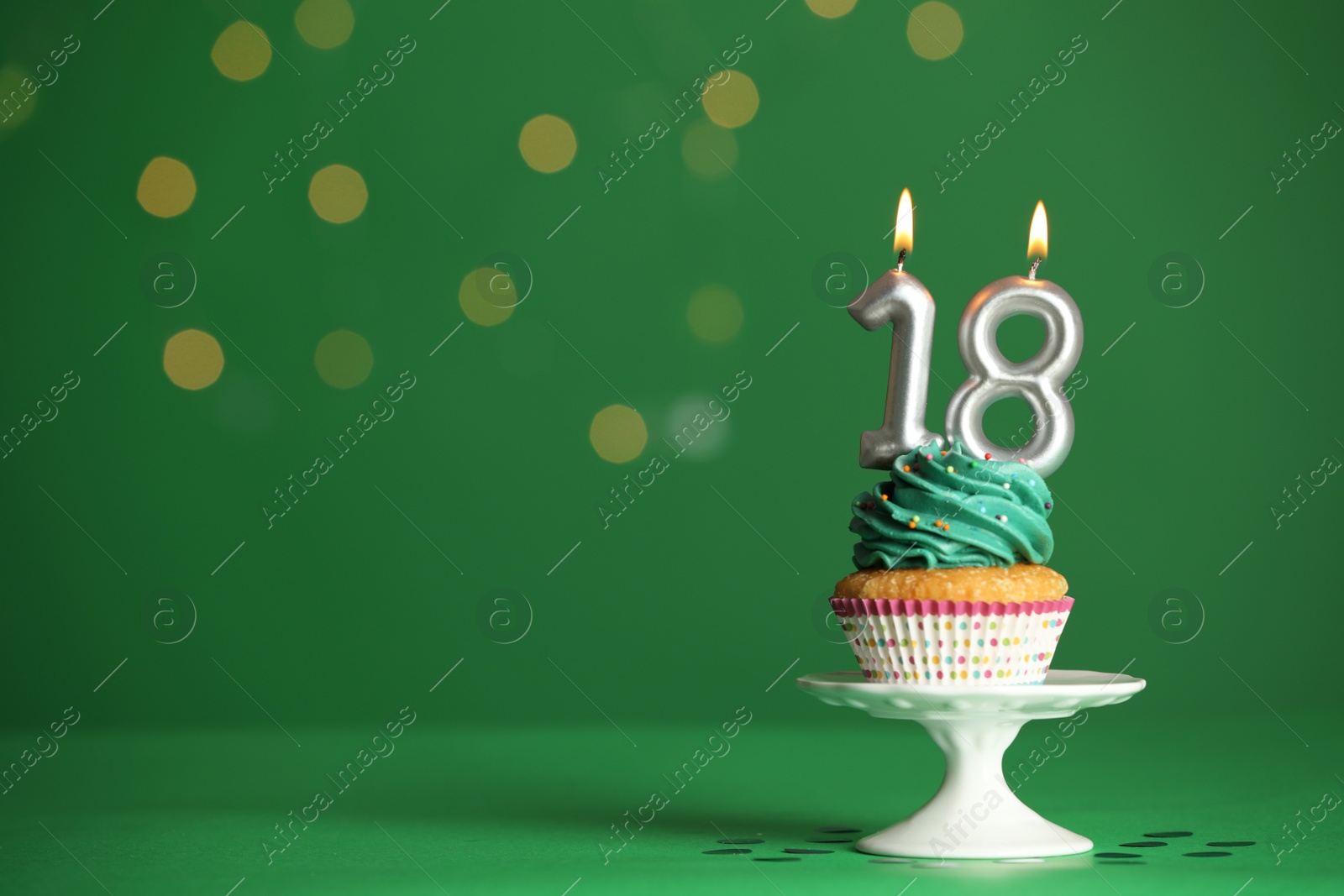 Photo of Coming of age party - 18th birthday. Delicious cupcake with number shaped candles on green background, space for text