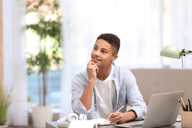 African-American teenage boy dreaming while doing homework at table in room