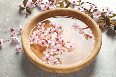 Bowl with water and blossoming flowers on grey background