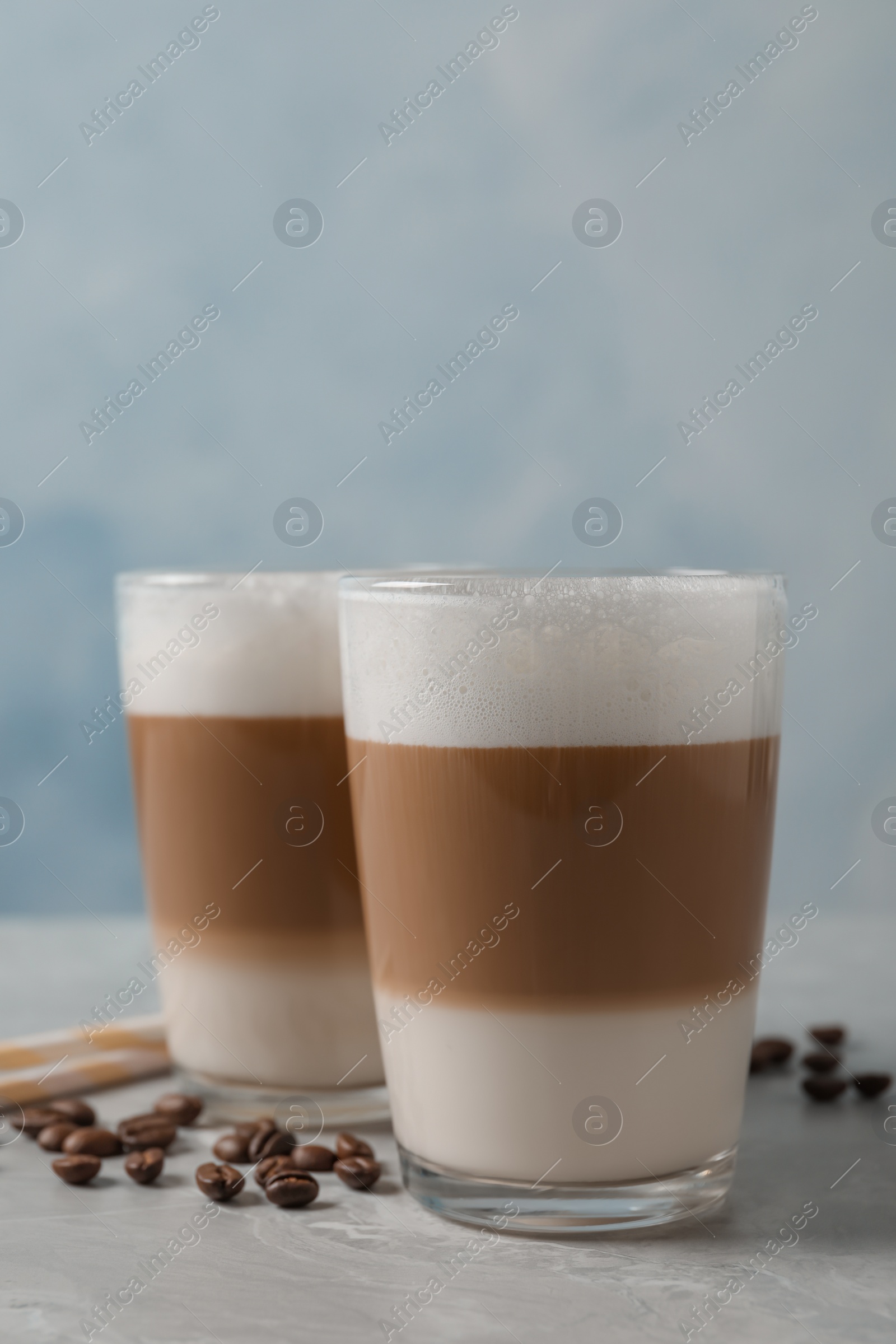 Photo of Glasses of delicious layered coffee and beans on grey marble table against light background, space for text