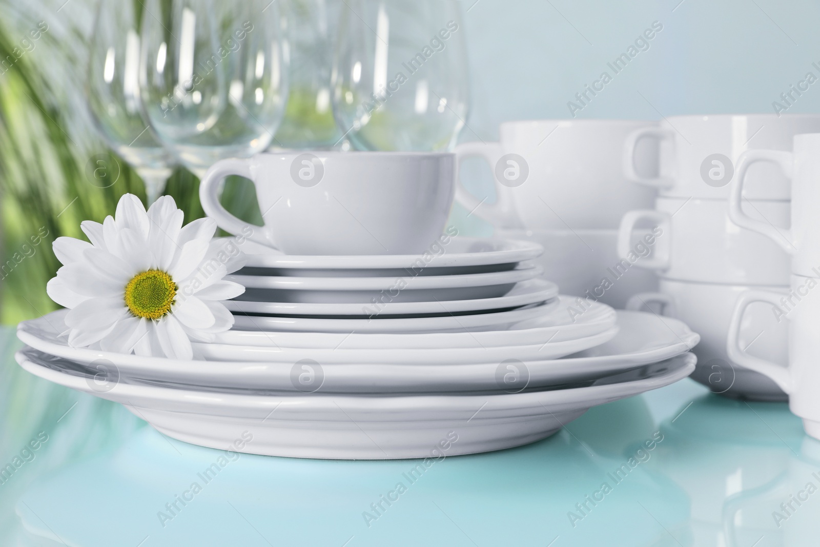 Photo of Set of clean dishware and flower on light blue table, closeup