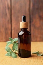 Photo of Bottle of mint essential oil and fresh herb on wooden table