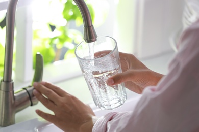 Photo of Woman pouring water into glass in kitchen, closeup