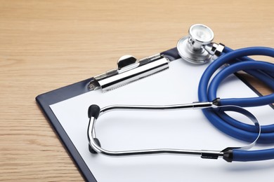 Photo of Clipboard with stethoscope on wooden table, closeup
