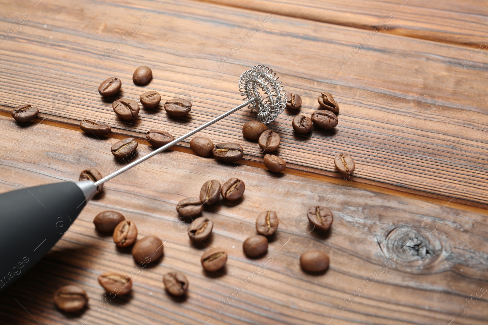 Photo of Black milk frother wand and coffee beans on wooden table, closeup