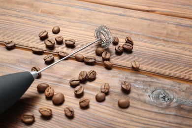 Photo of Black milk frother wand and coffee beans on wooden table, closeup