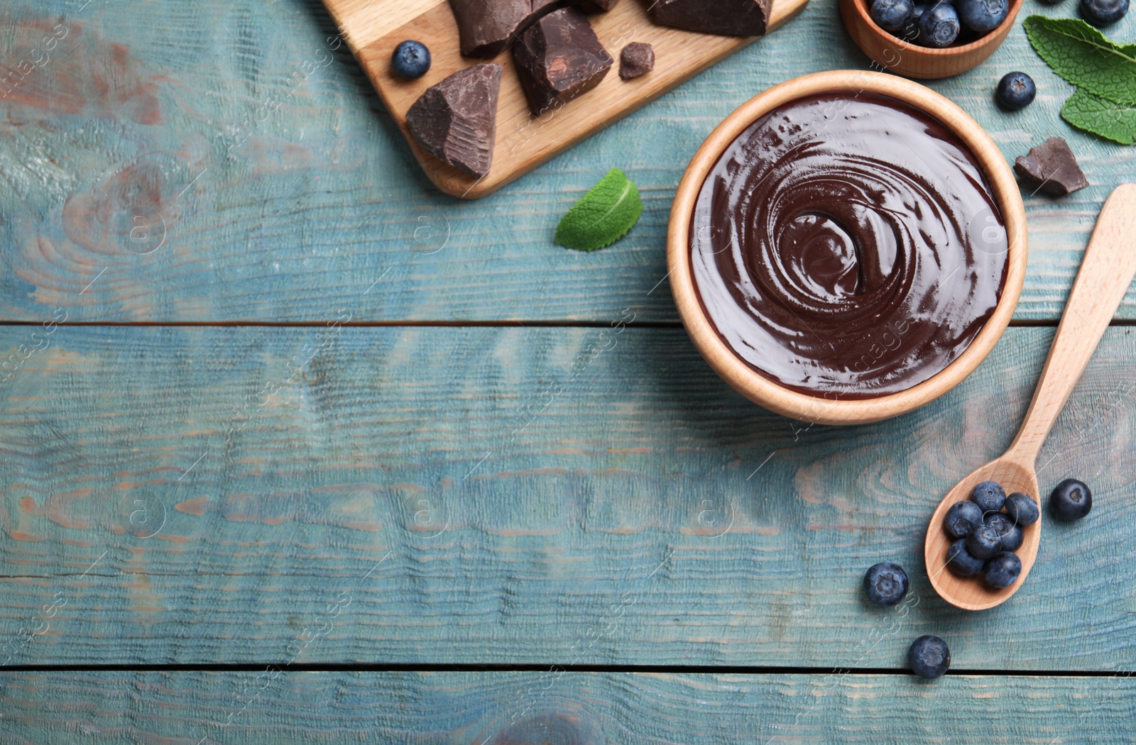 Photo of Delicious chocolate cream with blueberries and mint on light blue wooden table, flat lay. Space for text