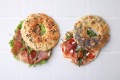 Tasty bagel sandwiches on white tiled table, flat lay