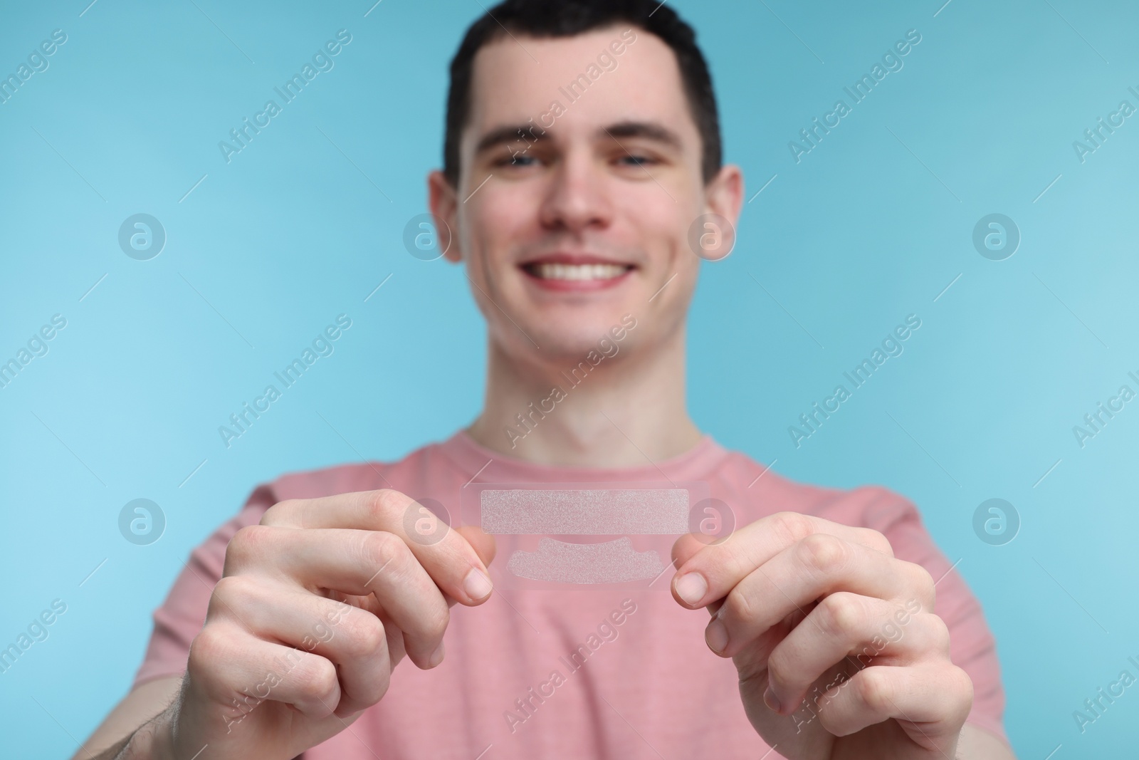 Photo of Young man with whitening strips on light blue background