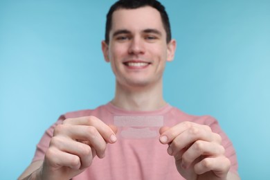 Young man with whitening strips on light blue background