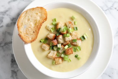 Tasty potato soup with croutons and green onion in bowl on white marble table, top view