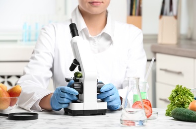Photo of Scientist inspecting broccoli with microscope in laboratory, closeup. Poison detection