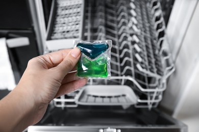 Photo of Woman putting detergent pod into open clean modern empty automatic dishwasher machine in kitchen, closeup
