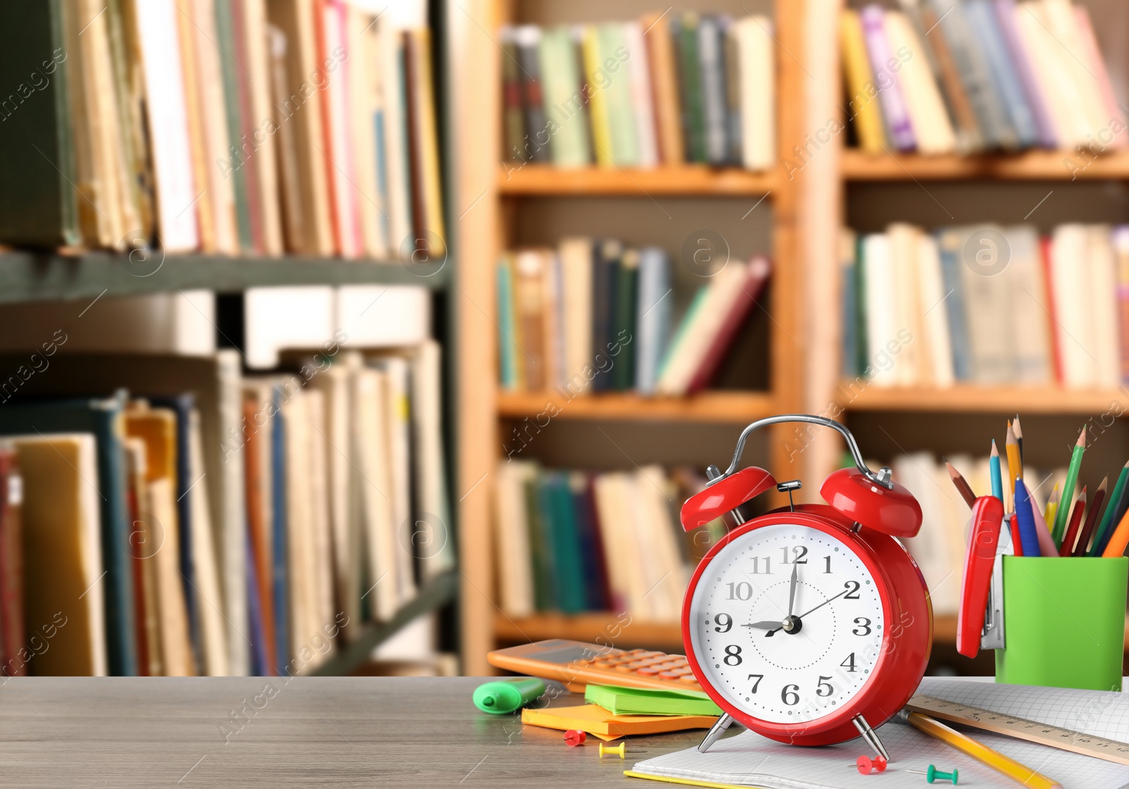 Image of Red alarm clock and different stationery on wooden table in library, space for text