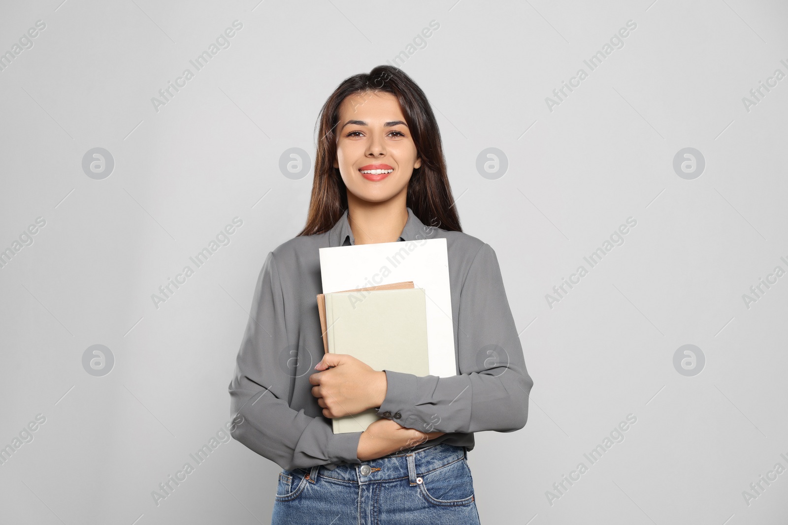 Photo of Happy young teacher with books on light grey background