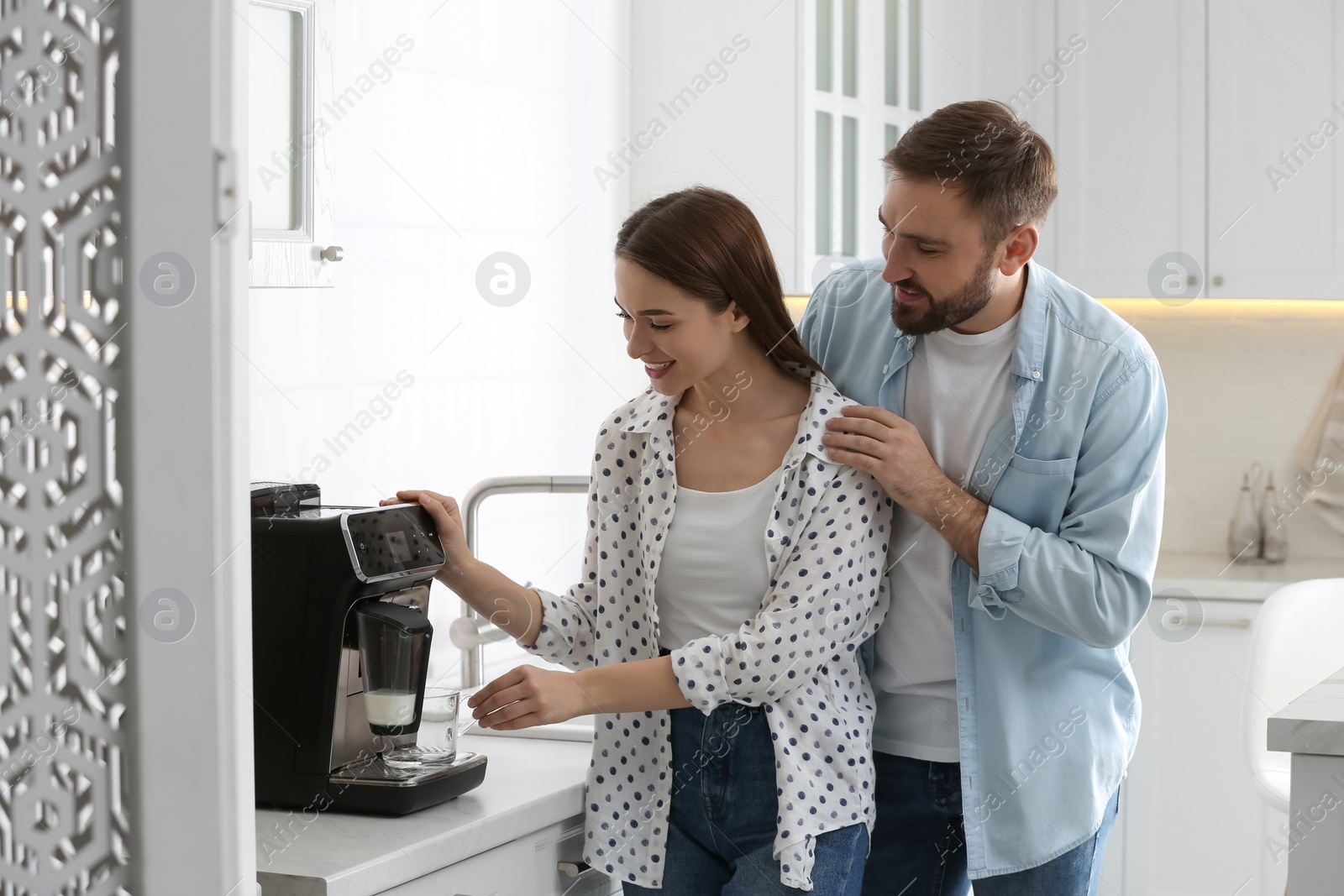 Photo of Happy couple preparing fresh aromatic coffee with modern machine in kitchen