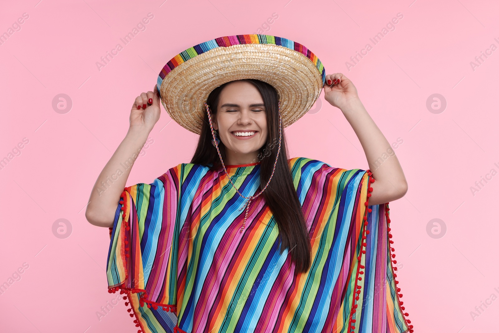 Photo of Young woman in Mexican sombrero hat and poncho on pink background
