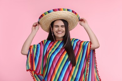 Young woman in Mexican sombrero hat and poncho on pink background